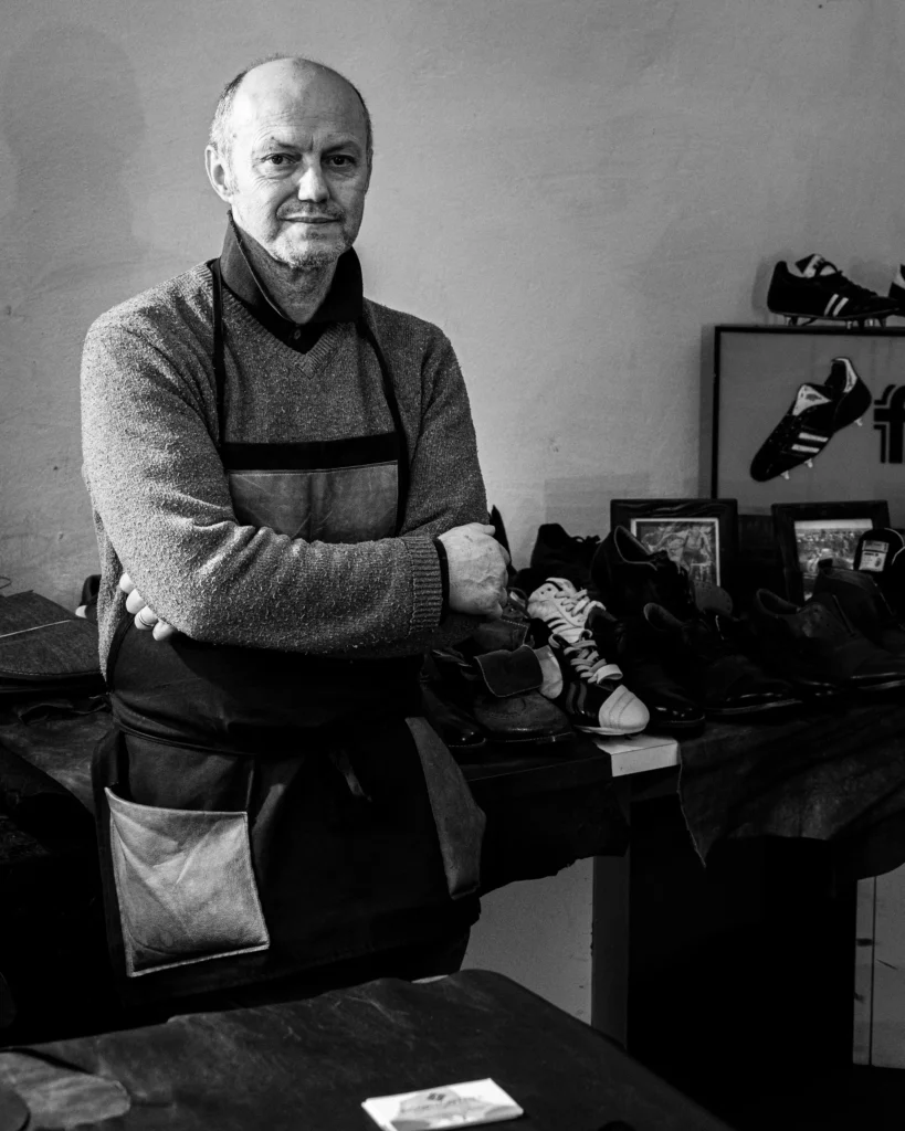 Portrait eines Schuhmachers in Arbeitskleidung vor gefertigten Schuhen